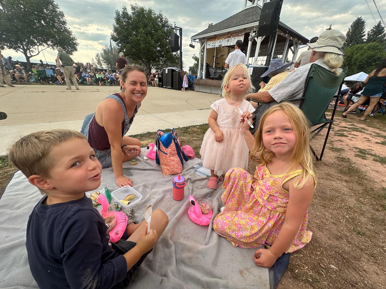Lizi sitting on a picnic blanket with her three children at an outdoor concert