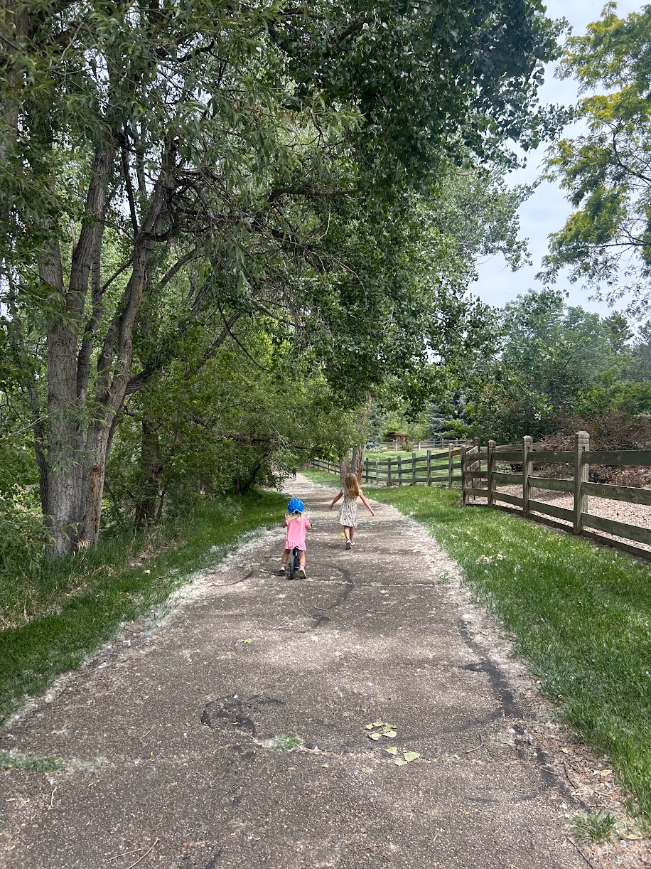 Ellie riding her bike and Emma walking ahead on a tree-lined path
