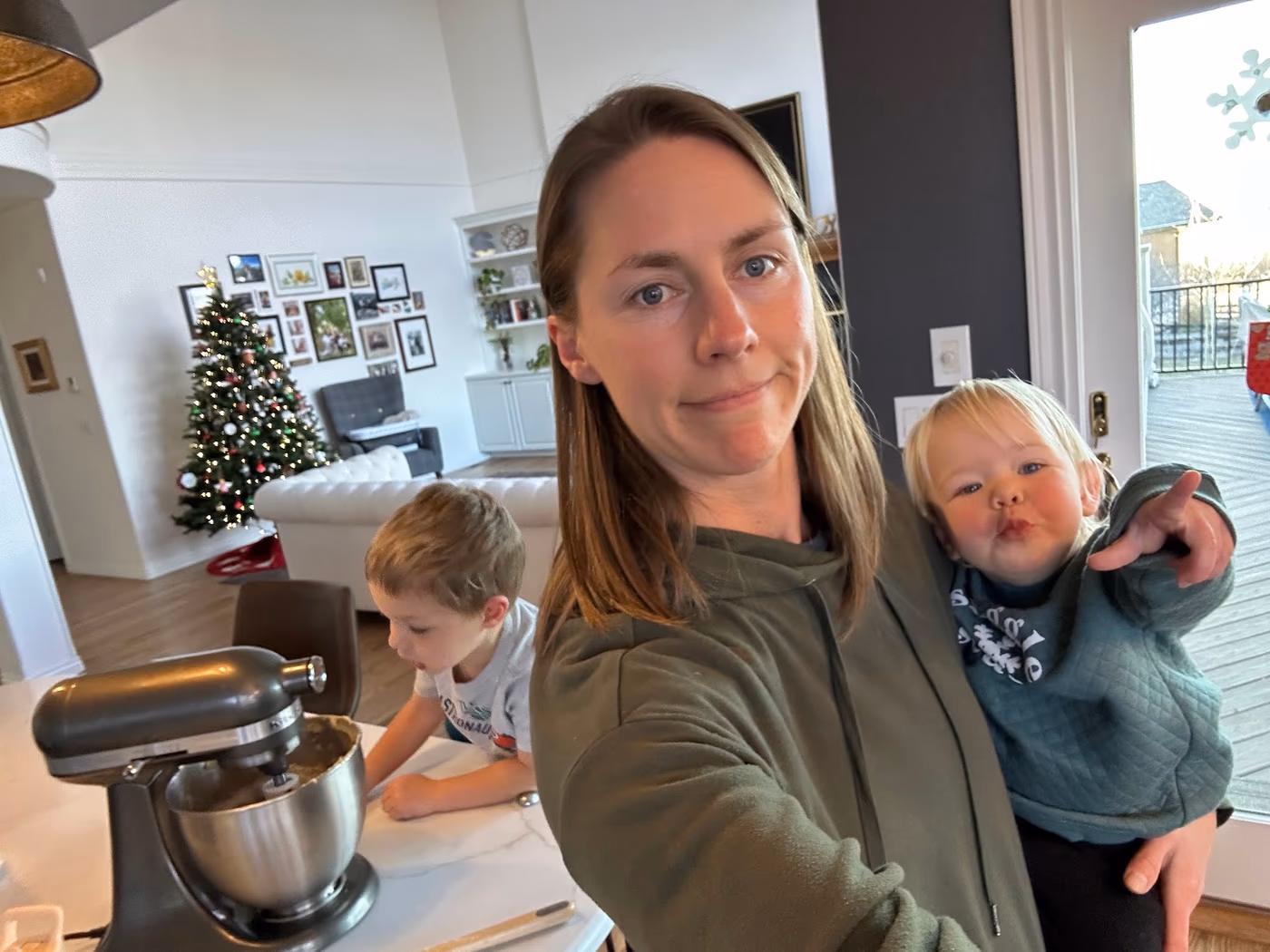 Lizi holding Ellie in the kitchen while Cooper bakes beside the mixer